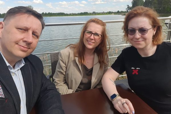 Troje uczestników robi wspólne selfie przy stole nad jeziorem